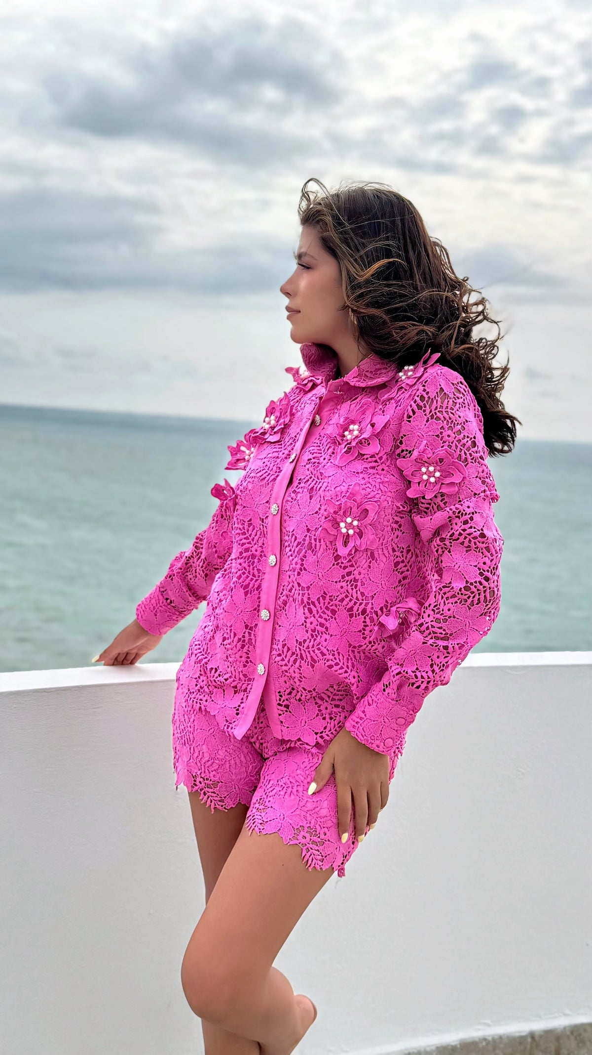 Conjunto Exotica de encaje fucsia con camisa de flores en relieve, perlas y short a juego frente al mar.