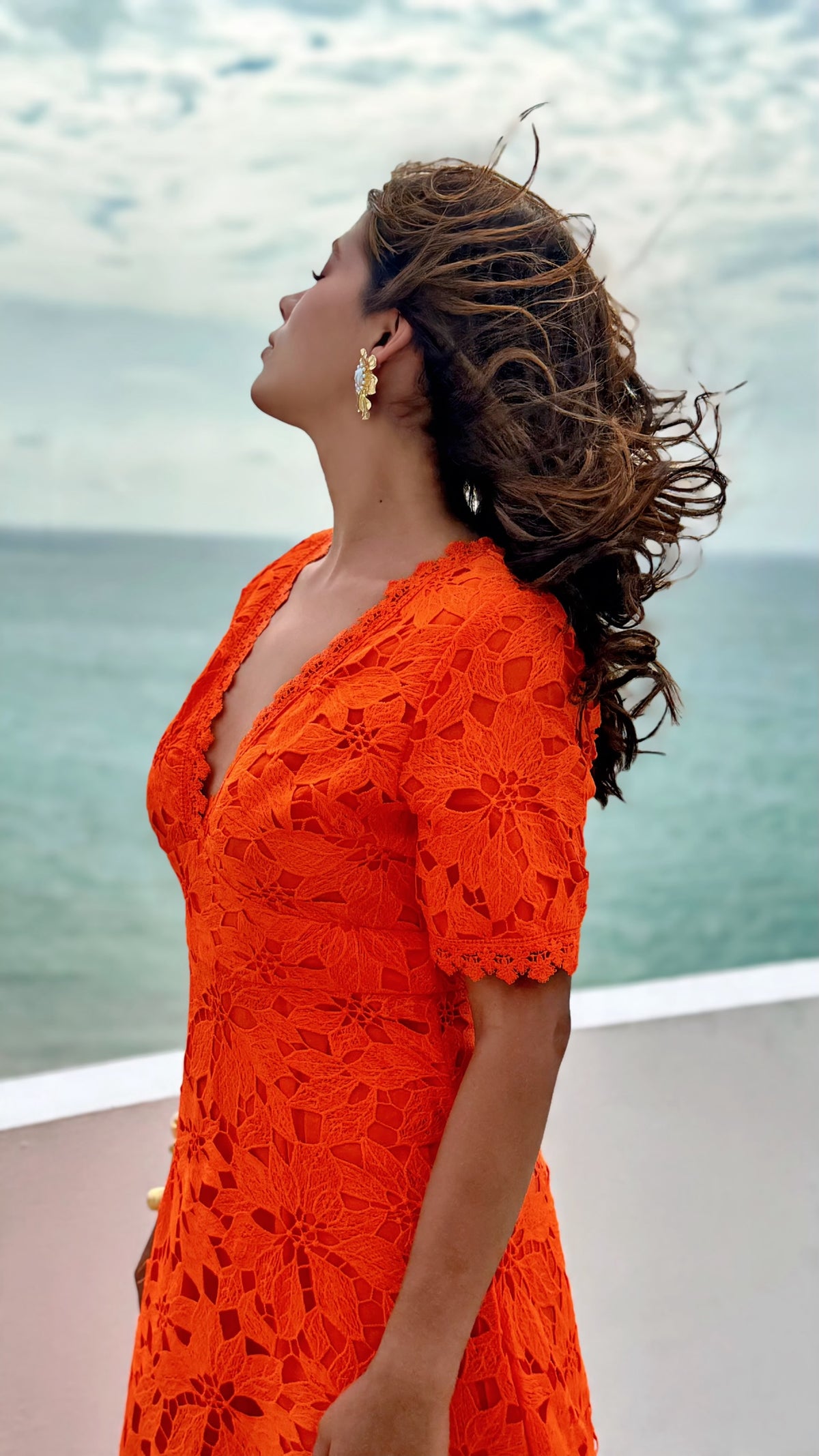 Exotica vibrant orange floral lace midi dress with V-neck and short sleeves worn by a woman by the ocean