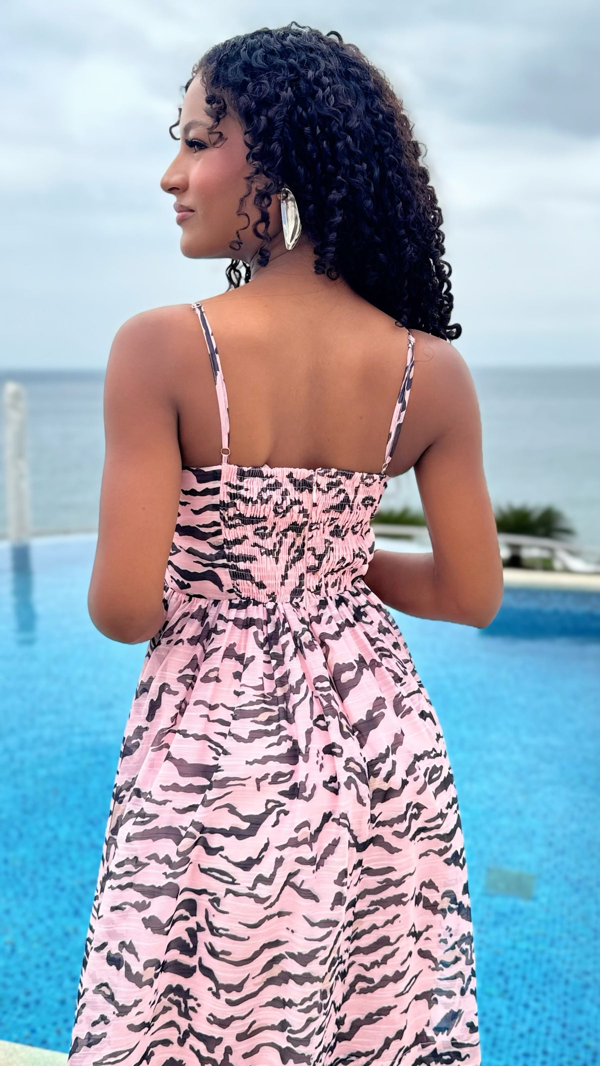 Exotica sleeveless midi dress in pink and black abstract animal print with a smocked back, worn by a model by a pool.